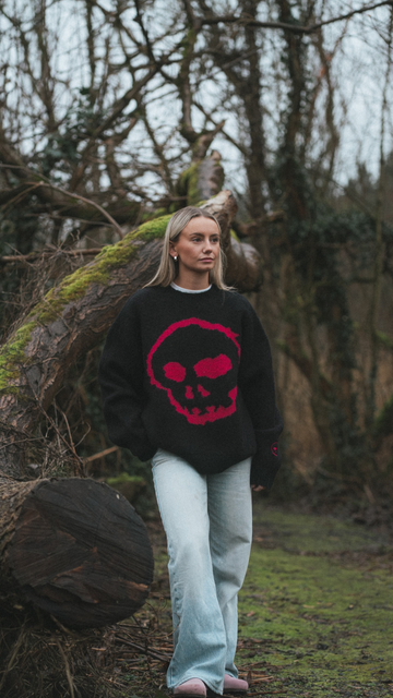 Person wearing a black sweater with a red skull design in a forest setting