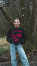Person wearing a black sweater with a pink skull design in a forest setting