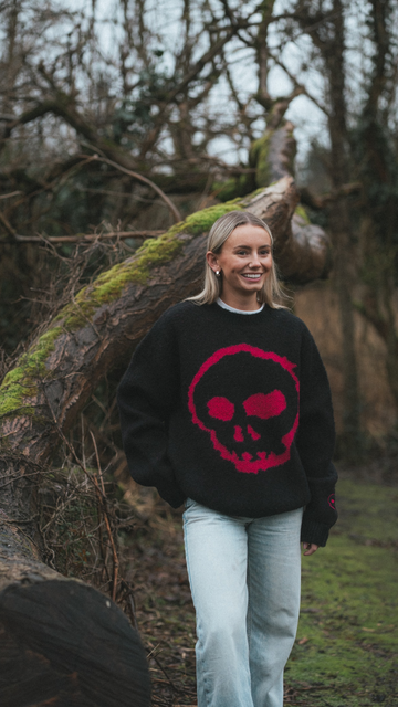 Person wearing a black sweater with a red skull design in a forest setting