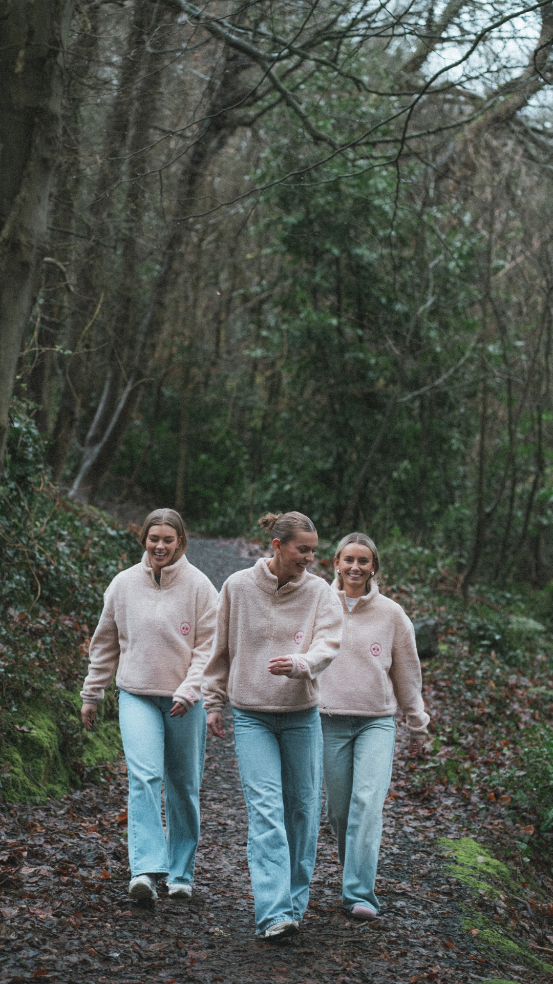 Three women walking together on a forest path wearing matching outfits.
