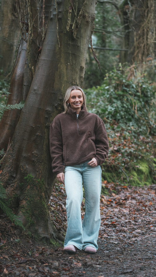 Woman standing beside a tree wearing a brown fleece cropped in length. 