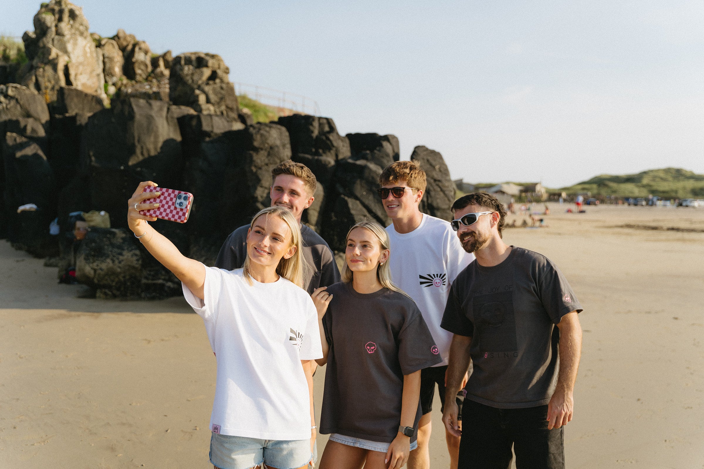Woman wearing a black sweatshirt with a small pink logo on a beach.slider_item_3jNbpH