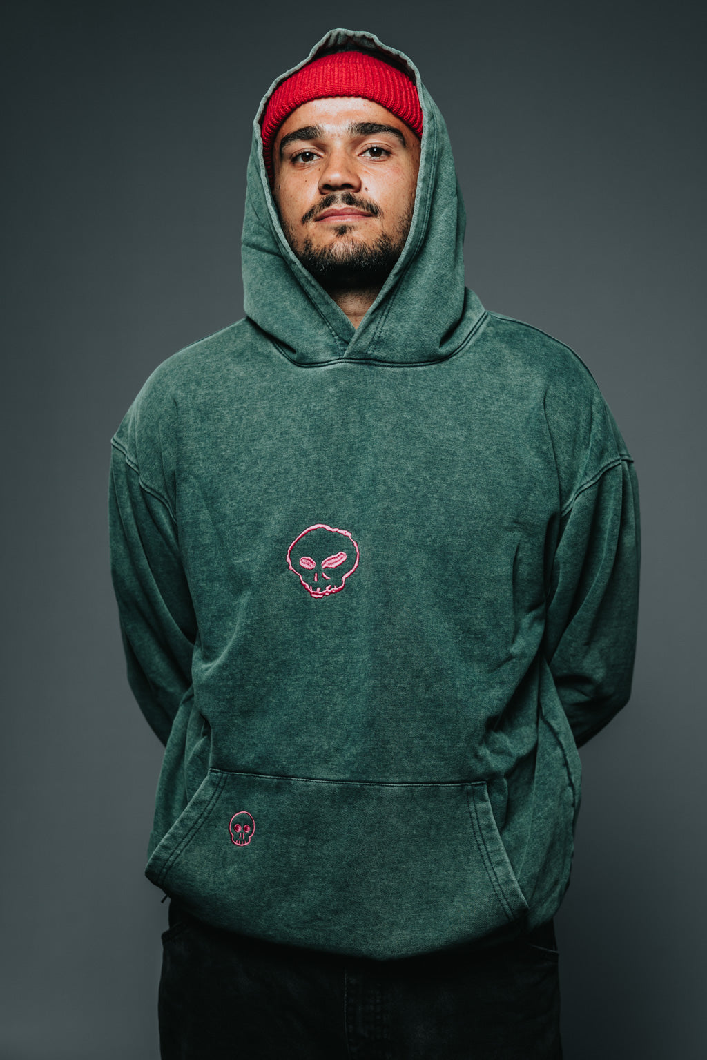 Person wearing a green hoodie with a pink skull design on a gray background