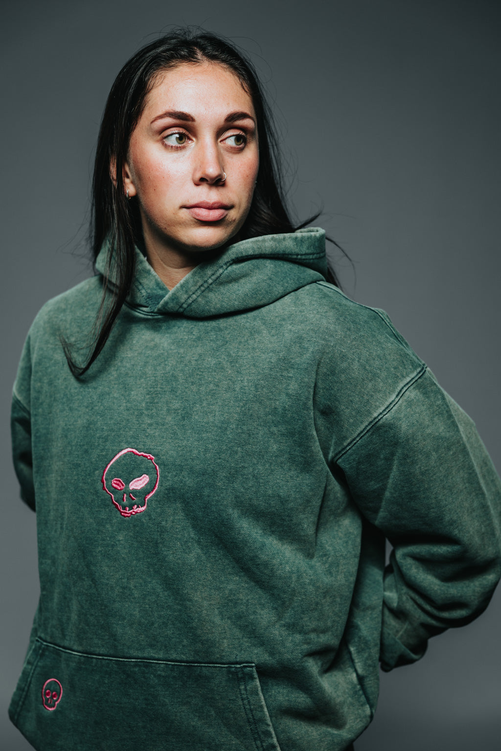 Person wearing a green hoodie with a pink skull design on a gray background