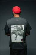 Person wearing a dark t-shirt with a graphic design on the back against a dark background