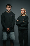 Two people wearing black sweatshirts with a small logo on a dark background