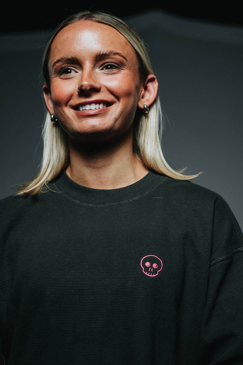 Person wearing a black sweatshirt with a small logo on a gray background