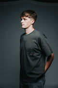 Man wearing a dark gray t-shirt with text and logos on a plain background