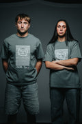 Two people wearing matching gray t-shirts with a logo on a dark background