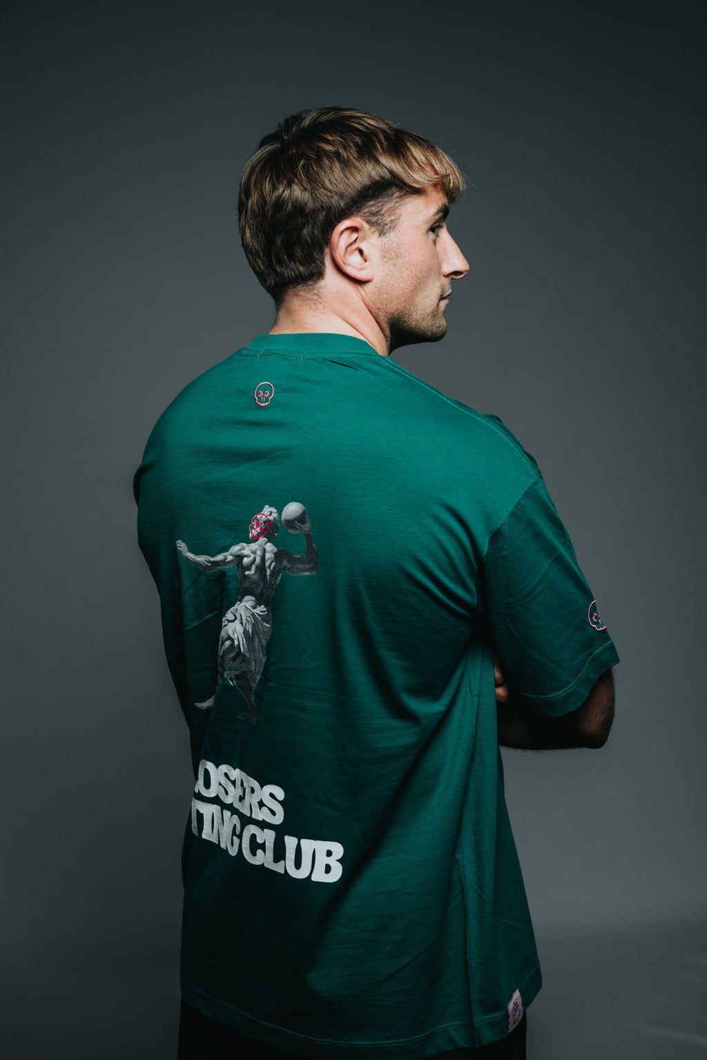 Person wearing a green t-shirt with a small logo on a dark background