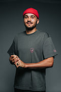 Man wearing a red beanie and dark t-shirt with logos on a gray background
