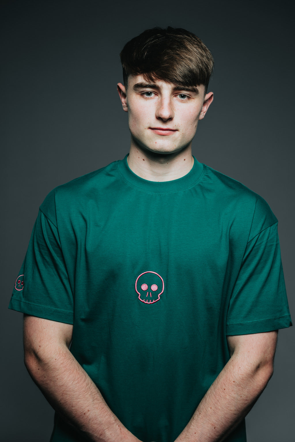 Person wearing a green t-shirt with a small logo on a dark background