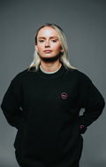 Person wearing a black sweatshirt with a small logo on a gray background