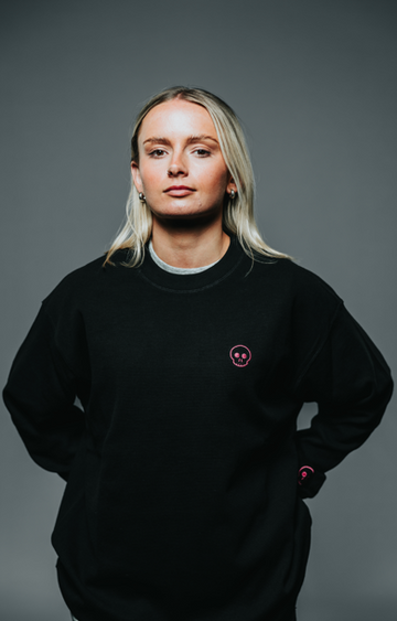 Person wearing a black sweatshirt with a small logo on a gray background