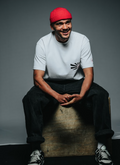 Man wearing a red beanie and white t-shirt sitting on a box against a gray background